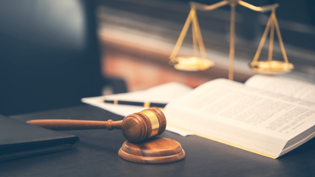 A gavel, open book, and a gold scale of justice on a desk